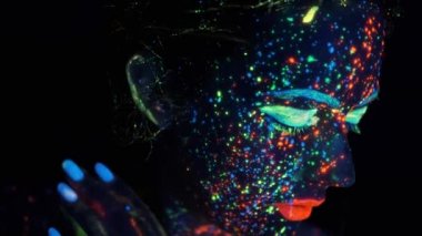 ultraviyole ışıkta genç bir kadının portresi. modelin yüzü parlayan renklerle boyanmıştır.