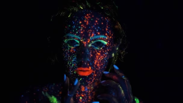 Modelová žena v neonové světelné, fluorescenční make-up. portrét dívky v neonové světelné světlu. obličej vymalovaný zář v tmavé malby. — Stock video