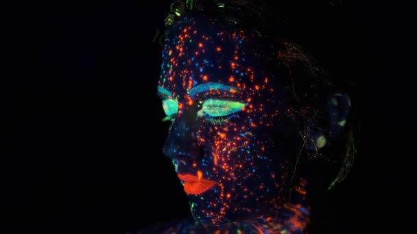 Sötétfestékkel festett arcú arc. Divatmodell nő neonfények pózol a stúdióban, portré gyönyörű lány,. — Stock videók