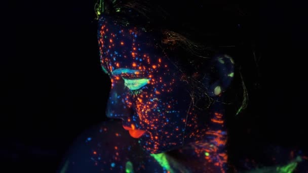 ネオンの光の中の少女の肖像画。暗いペンキで輝きを放つ顔. — ストック動画