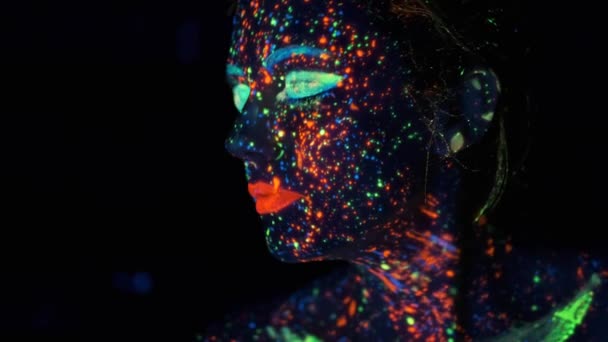 Retrato de close-up em luz ultravioleta. rosto pintado com brilho na tinta escura . — Vídeo de Stock