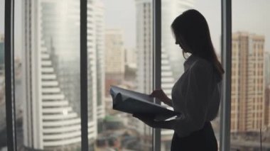 Bir klasör için ellerini gazetelerde çekici bir kızla silüeti. pencerenin yakınındaki ofiste genç iş kadını standları