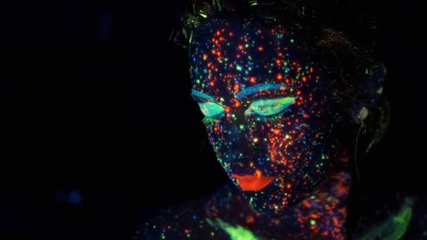 Ultraviyole ışıkta yakın çekim portre. koyu boya parıltı ile boyanmış yüz. — Stok video