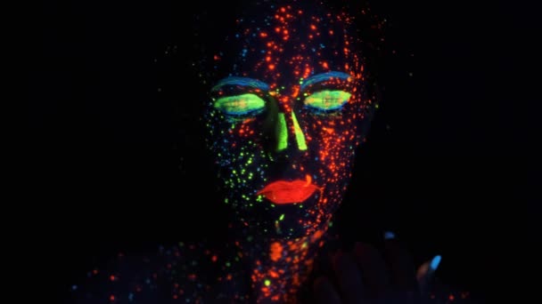 Neonfärg i ansiktet. Porträtt av en flicka målad med glödande färg — Stockvideo