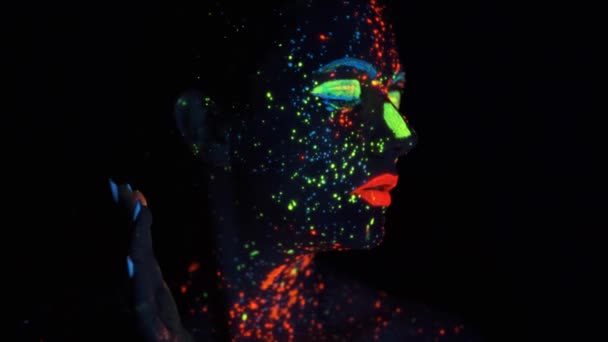 Verf gloeien in ultraviolet licht. Portret van een meisje geschilderd met gloeiende verf. — Stockvideo