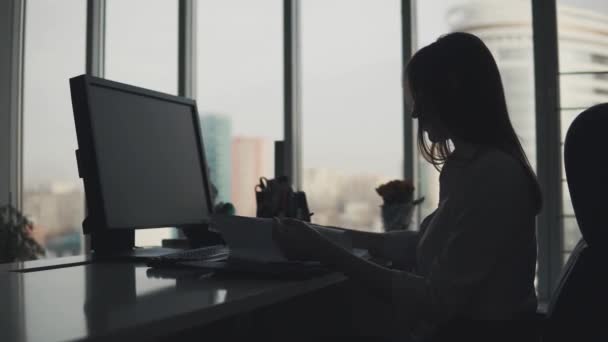 Giovane donna lavora con i documenti a tarda sera in ufficio. silhouette di una donna d'affari sul posto di lavoro — Video Stock