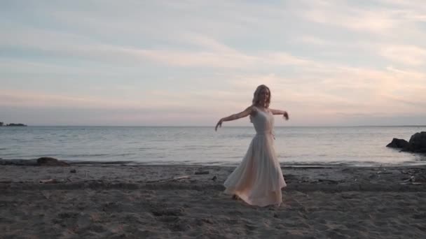 Meisje in een vloeiende jurk dansen bij de zee bij zonsondergang. — Stockvideo