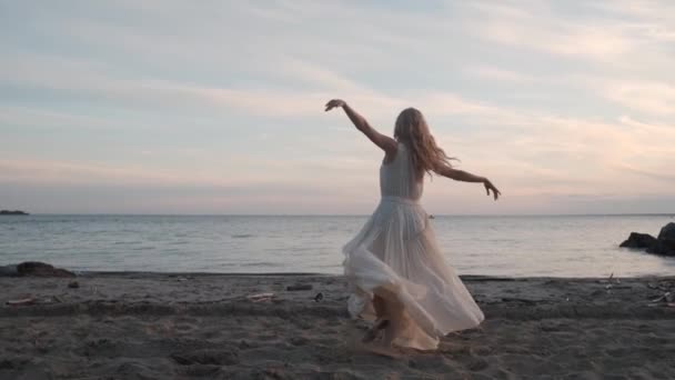 Ballerina in einem fließenden Kleid, das bei Sonnenuntergang am Meer tanzt. — Stockvideo