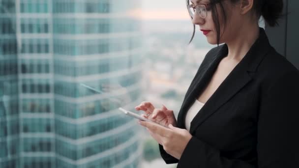 穿着西装的年轻女子使用智能手机。摩天大楼背景上一位女商人的肖像. — 图库视频影像