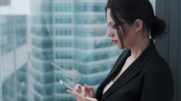 Egy üzleti nő portréja, mobiltelefonnal a modern épületek hátterével szemben. — Stock videók