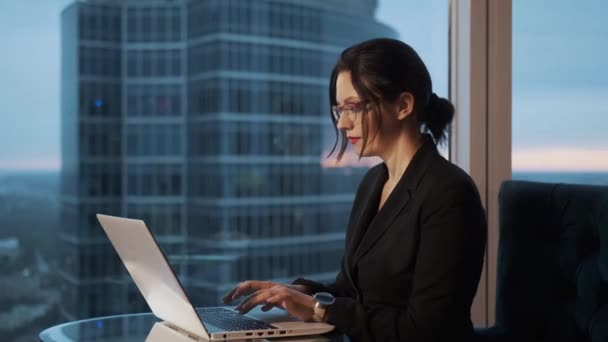 Портрет деловой женщины в очках в офисе. девушка сидит за столом и работает на ноутбуке — стоковое видео