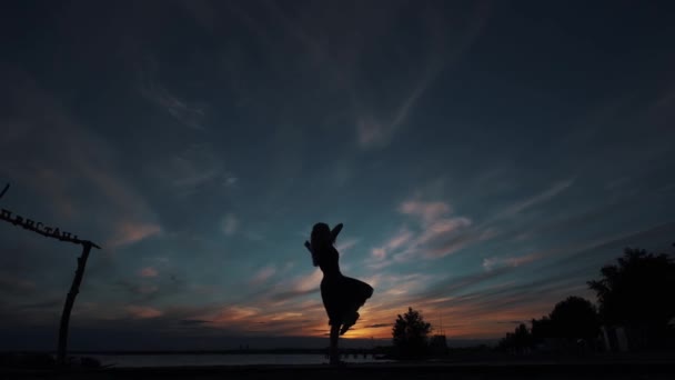 Σιλουέτα μιας μπαλαρίνας ενάντια στον ουρανό του ηλιοβασιλέματος. το κορίτσι όμορφα χορεύει στέκεται σε μύτες ποδιών. — Αρχείο Βίντεο
