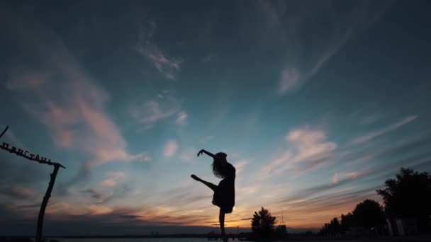 Σιλουέτα μιας μπαλαρίνας που χορεύει ενάντια στον ουρανό του ηλιοβασιλέματος. — Αρχείο Βίντεο