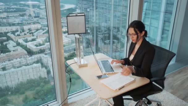 Unga affärskvinna som arbetar på en bärbar dator i ett modernt kontor ligger på den övre våningen i en skyskrapa. — Stockvideo