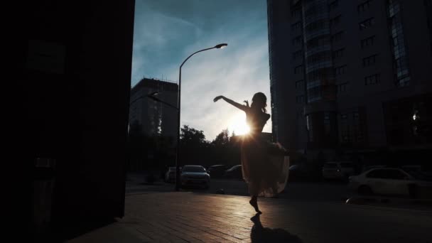 屋外で踊るフライングドレスのバレリーナのシルエット。都市の建物を背景に踊るスリムな女の子. — ストック動画