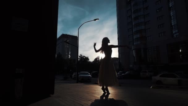 Silueta de una bailarina con un vestido volador bailando al aire libre. chica delgada bailando sobre el fondo de los edificios urbanos . — Vídeos de Stock