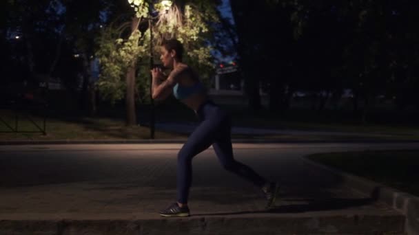 Спортсмен делает приседания на тренировке в вечерней Праке. девушка в спортивной одежде поезда поздно ночью на открытом воздухе — стоковое видео