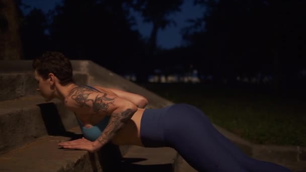 Chica musculosa haciendo flexiones en el parque nocturno. atleta en el entrenamiento de la noche al aire libre — Vídeos de Stock