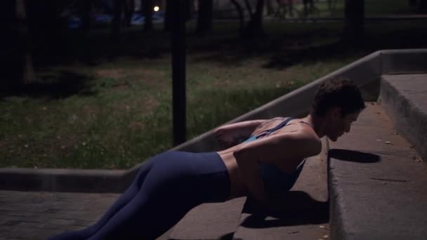 Chica musculosa haciendo flexiones en el parque nocturno. atleta en el entrenamiento de la noche al aire libre — Vídeo de stock