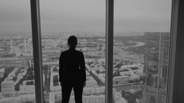 Mujer de negocios se encuentra cerca de una gran ventana en un piso alto de un rascacielos . — Vídeo de stock