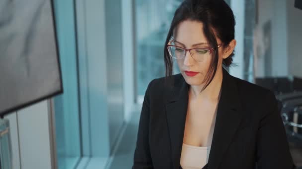 職場でのビジネススーツを着た若い女性のクローズアップ肖像画。オフィスの窓のそばに座っているコンピュータで働くビジネスウーマン — ストック動画