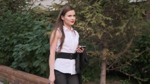 Unga affärskvinna går i sommarstaden. Flickan tog av sig jackan och njuter av det vackra vädret. — Stockvideo