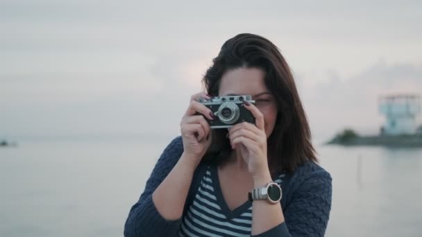 Retrato de uma menina com uma câmera retro. jovem mulher tira fotos em uma câmera vintage pelo oceano — Vídeo de Stock