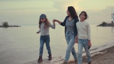 aile dışarıda birlikte vakit geçirir. genç anne gün batımında deniz kıyısında çocuklarıyla birlikte yürüyor
