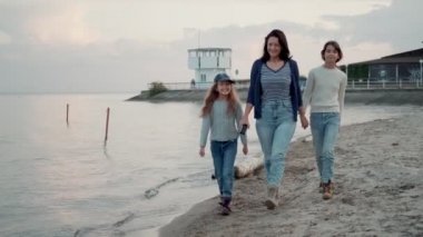 aile gün batımında deniz kıyısında yürür. Genç bir anne çocuklarıile eğleniyor