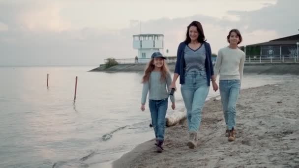 Família caminha ao longo da praia ao pôr do sol. uma jovem mãe está se divertindo com seus filhos — Vídeo de Stock