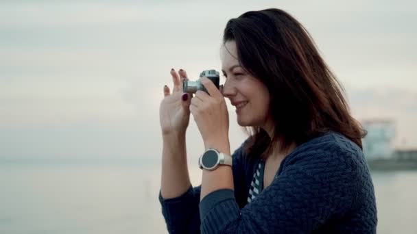Mujer joven toma fotos en una cámara retro al aire libre . — Vídeo de stock
