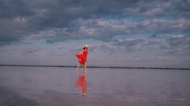 çırpınan bir elbise genç kadın gökyüzünün yansıtıldığı bir tuz gölü boyunca çalışır.