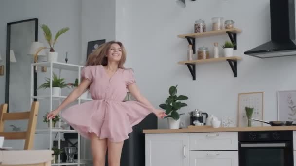 Chica despreocupada bailando divertido en la cocina. joven mujer está girando en un vestido en casa — Vídeos de Stock