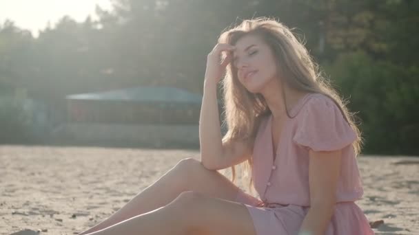 Aantrekkelijke jonge vrouw geniet van de warme stralen van de zon terwijl zittend op de kust — Stockvideo