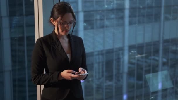 Zbliżenie portret kobiety biznesu z smartphone w dłoniach. Kobieta w kombinezon biznesowy stoi przez duże okno — Wideo stockowe