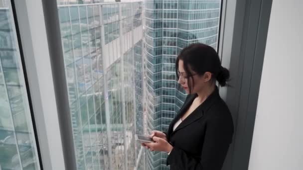 Портрет бизнесмена у большого окна на фоне небоскребов. молодая женщина использует мобильный телефон — стоковое видео