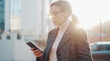 Kız dışarıda cep telefonu kullanıyor. Elinde akıllı telefon olan genç bir kadının portresi.