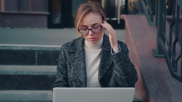 Gözlüklü ve ceketli çekici kız dışarıda dizüstü bilgisayar kullanıyor. — Stok video
