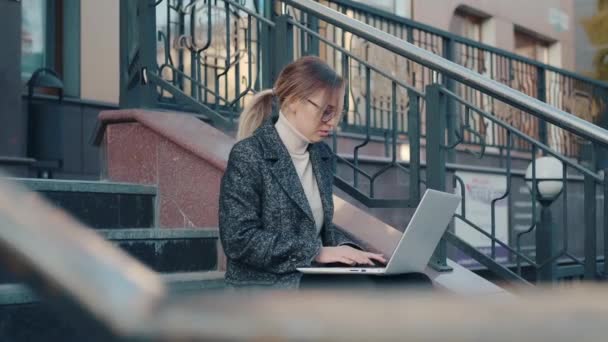 Retrato de una mujer de negocios trabajando en una computadora sentada en los escalones de un edificio de negocios — Vídeos de Stock