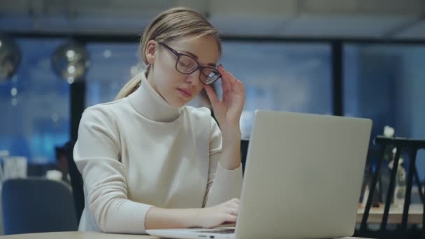 Young woman in glasses works on a laptop while sitting in an evening cafe — Stock Video