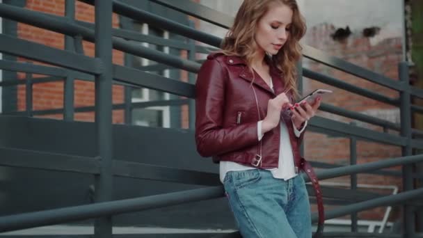 Mulher jovem na moda usa um telefone celular ao ar livre — Vídeo de Stock