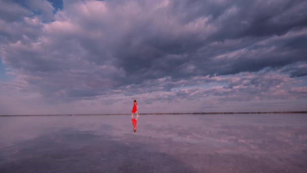Turist kız bulutlar yansıyan bir tuz gölü boyunca yürüyor. — Stok video
