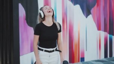 Renkli bir duvarın arkasında dans eden güzel, genç bir kız. Büyüleyici bir gülümsemesi olan genç bir kadın kulaklıkla müzik dinliyor.