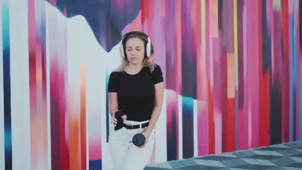 Vacker ung kvinna dansar roligt och bekymmerslöst mot bakgrund av en färgad vägg — Stockvideo