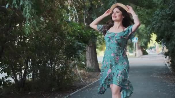 Joven camina por el callejón y sonríe alegremente. retrato de una joven con un sombrero que gira en un vestido largo — Vídeo de stock