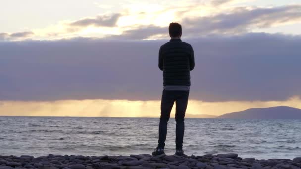 Silhouette di giovane uomo nella retroilluminazione in piedi sulla spiaggia — Video Stock