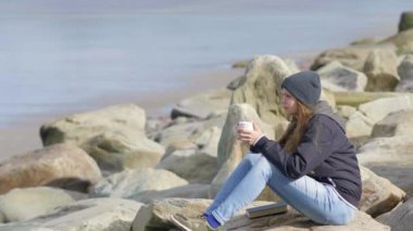 Genç kadın plajda bir fincan kahve ile oturuyor.