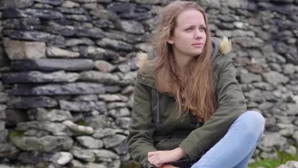 Молодая женщина сидит на земле - кажется, грустно — стоковое видео