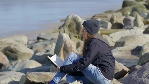 Chica joven y solitaria se sienta en la playa y lee un libro — Vídeos de Stock