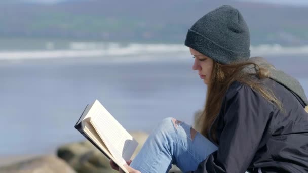 Flicka åtnjuter en bok vid vattnet — Stockvideo